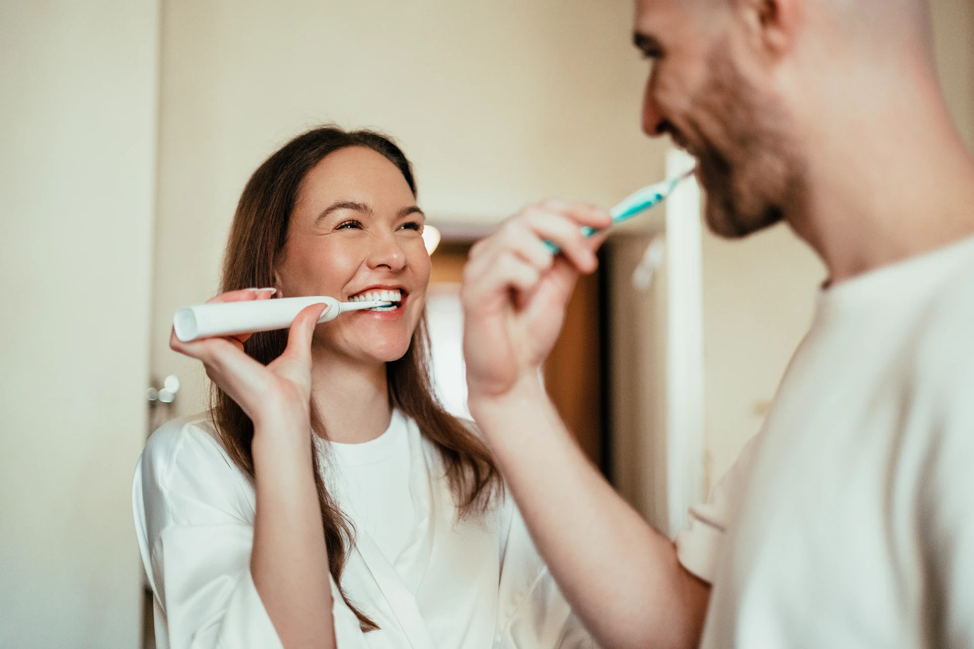 Smiling man and woman brushing their teeth together at home