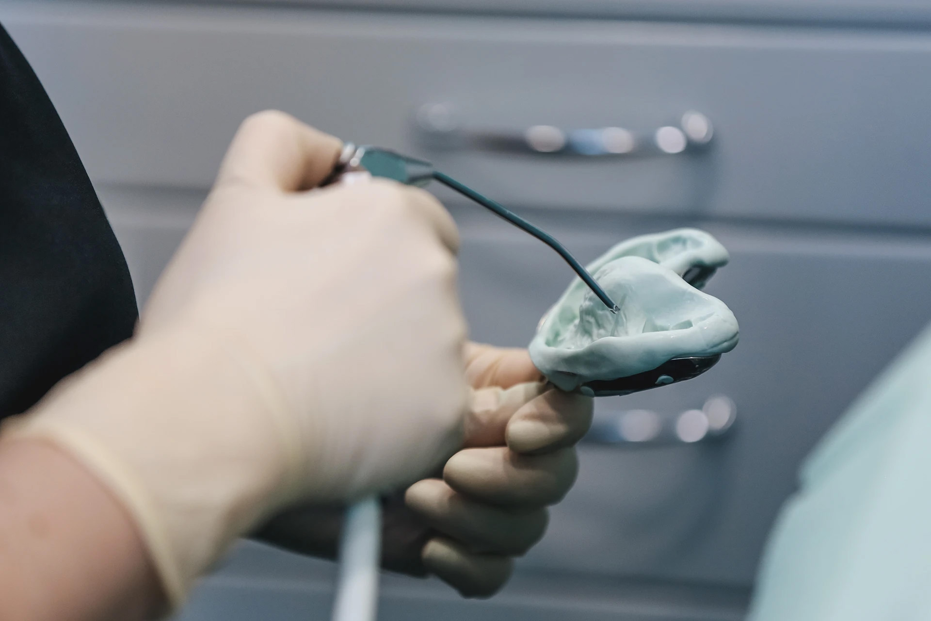 Gloved hand holding a green dental impression in a tray beside instruments