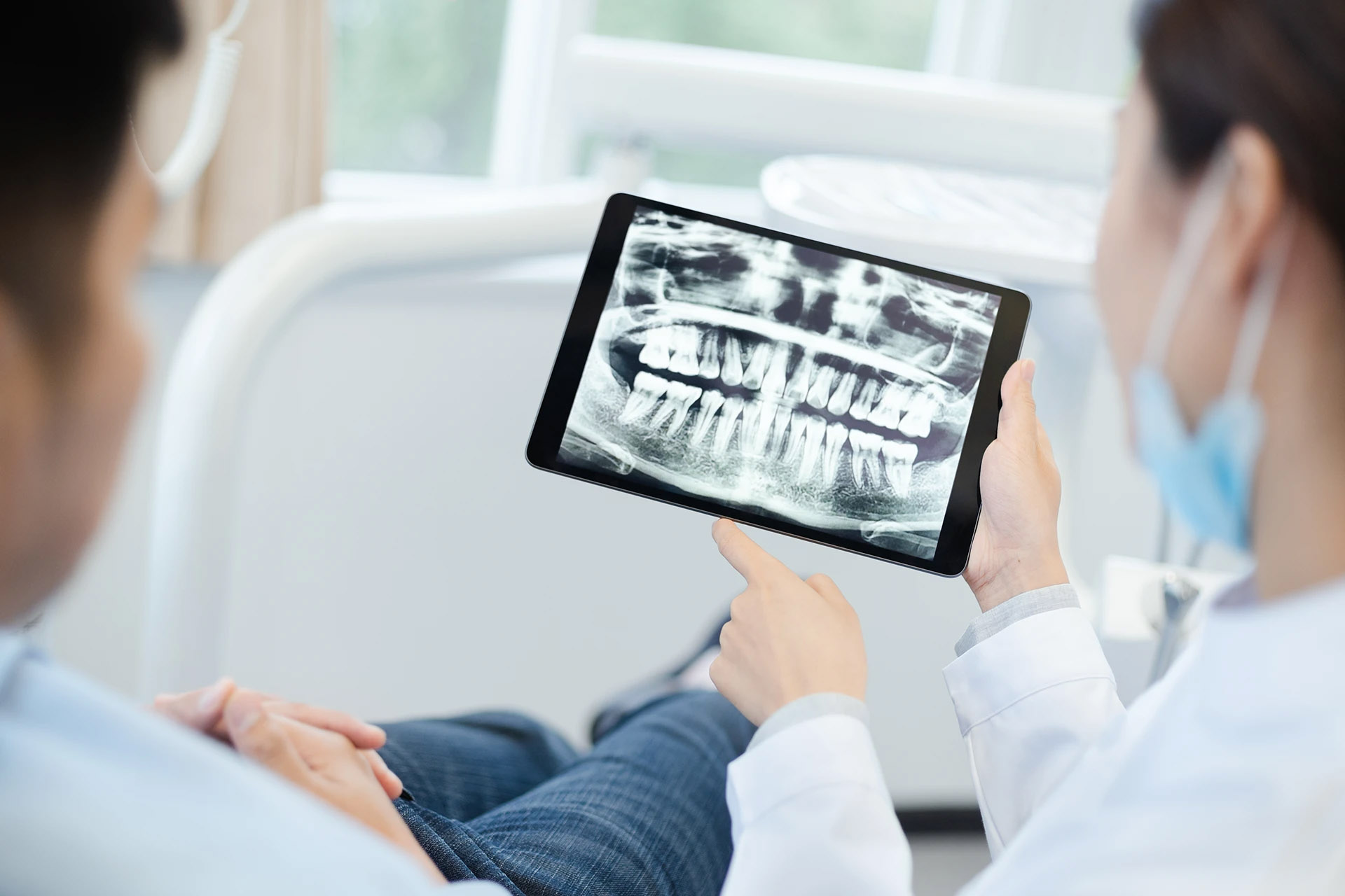 Dentist in a white coat showing a patient a panoramic dental X-ray on a tablet