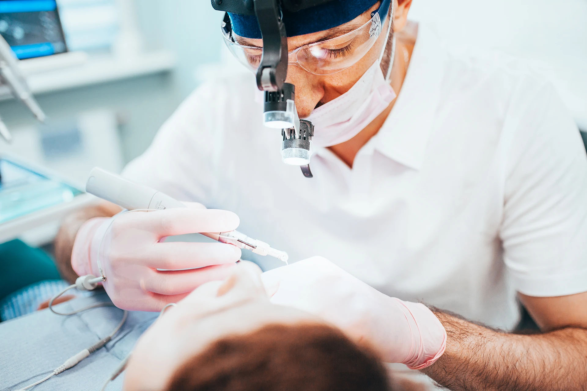 Focused dentist wearing magnifying loupes and a headlamp treating a patient with a handpiece