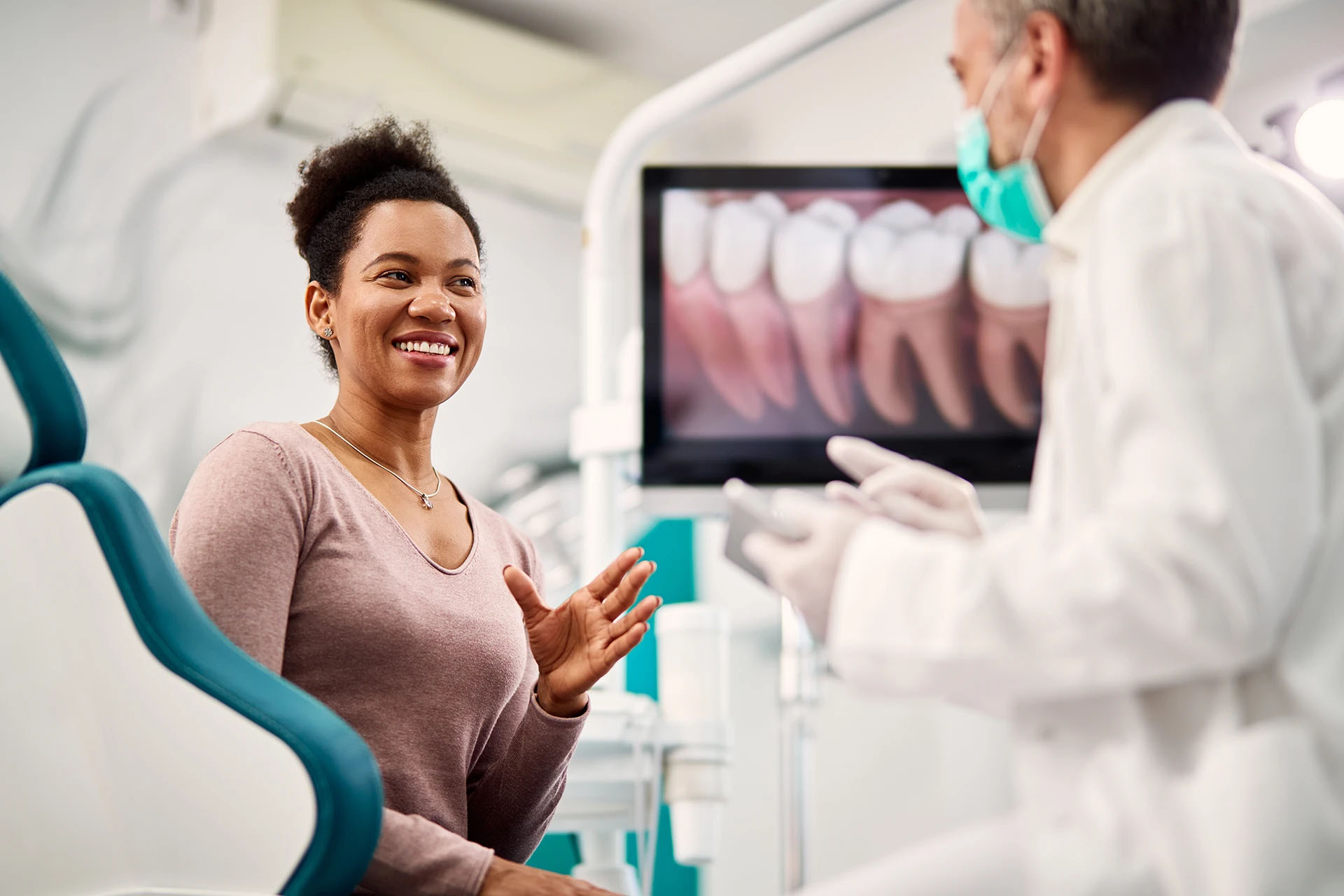 Smiling woman in a dental chair chatting with a masked dentist, an intraoral image of teeth on the monitor
