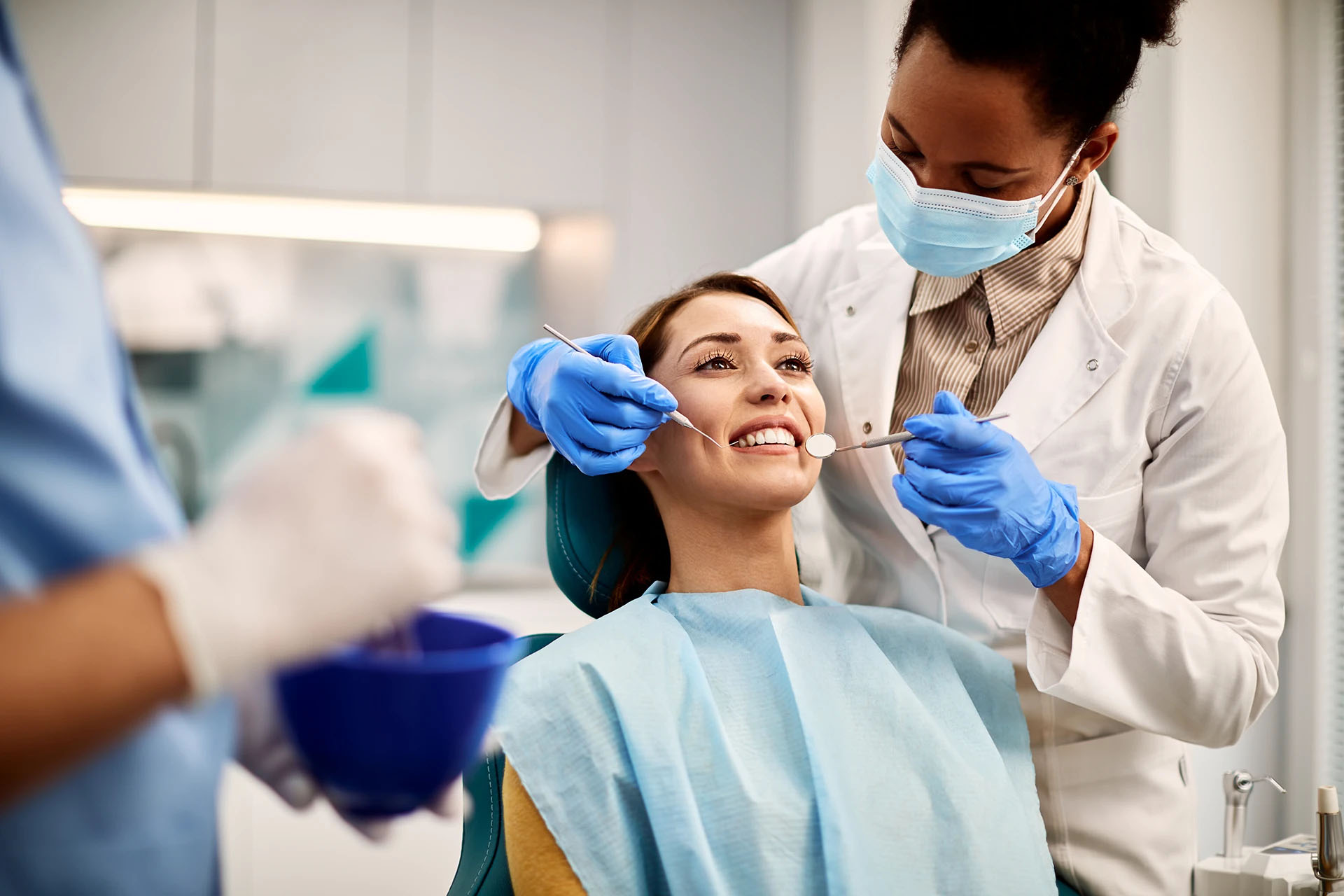 Smiling woman in a dental chair during a checkup as a masked female dentist examines her teeth