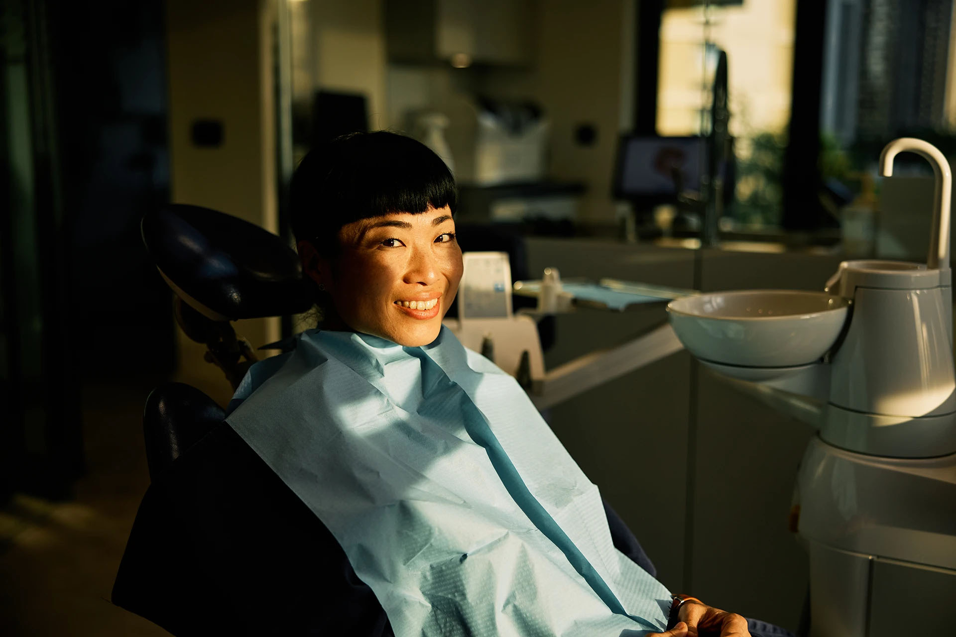 Smiling woman relaxing in a dental chair bathed in warm golden light