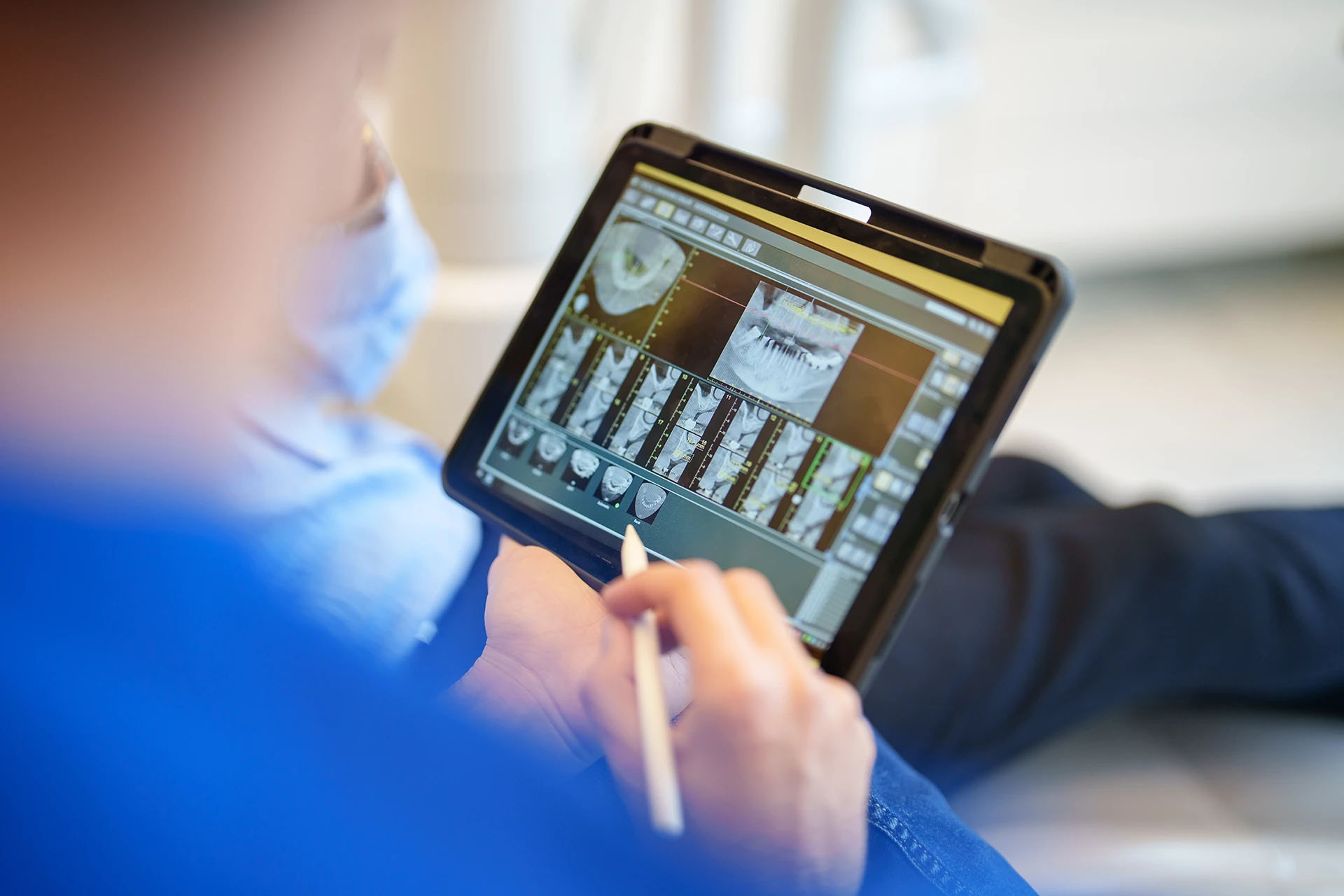 Masked dentist studying a 3D CBCT dental scan on a tablet for treatment planning