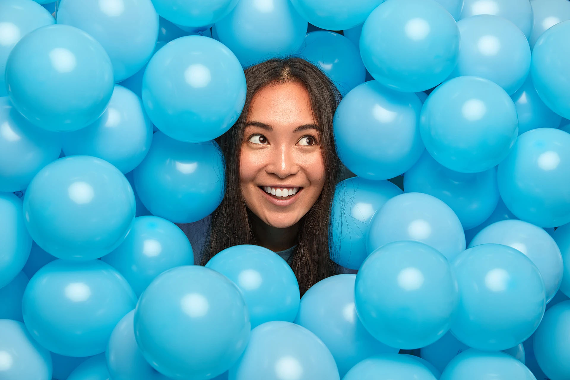 Smiling woman peeking through a wall of light blue balloons