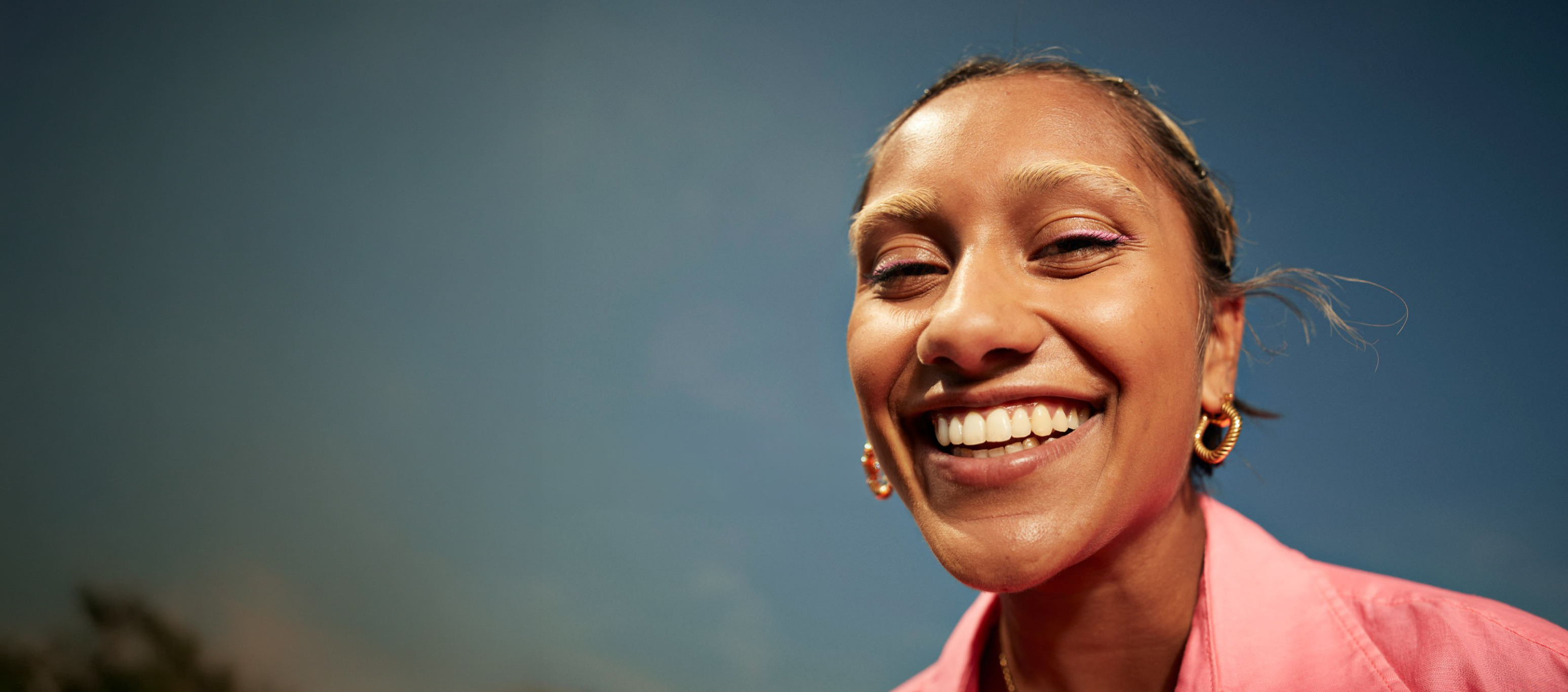 Studio portrait of a smiling woman in a pink shirt with a bright smile against a blue background