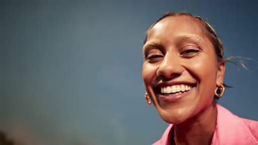 Studio portrait of a smiling woman in a pink shirt with a bright smile against a blue background
