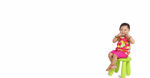 A baby seated stool white, against a green background