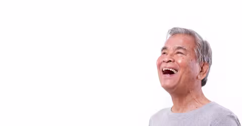 An older adult man laughing, against a white background