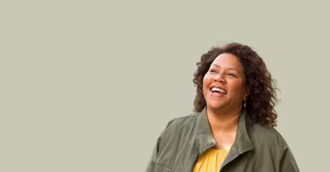 A woman green jacket laughing, against a olive background